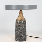 Grey marble Clérachic table lamp with its disc shade tilted to one side, shown with its cord on a white background.