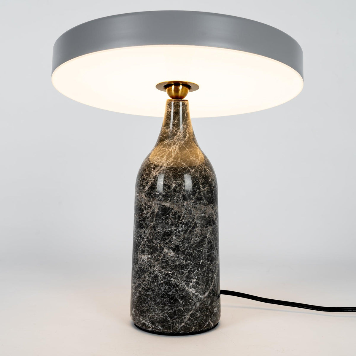 Grey marble Clérachic table lamp lit warm, its disc shade level above the glowing base on a plain background.
