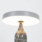 Close crop of the lit Clérachic table lamp, its grey disc shade glowing warm above the marble neck.