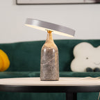 Grey marble Clérachic table lamp on a round wooden table beside a green velvet sofa and a cloud-shaped cushion.