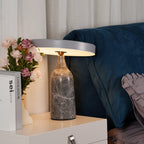 Angled lower against the roses and books, this Clérachic lamp's charcoal marble base and tilted disc shade glow warm on the table.