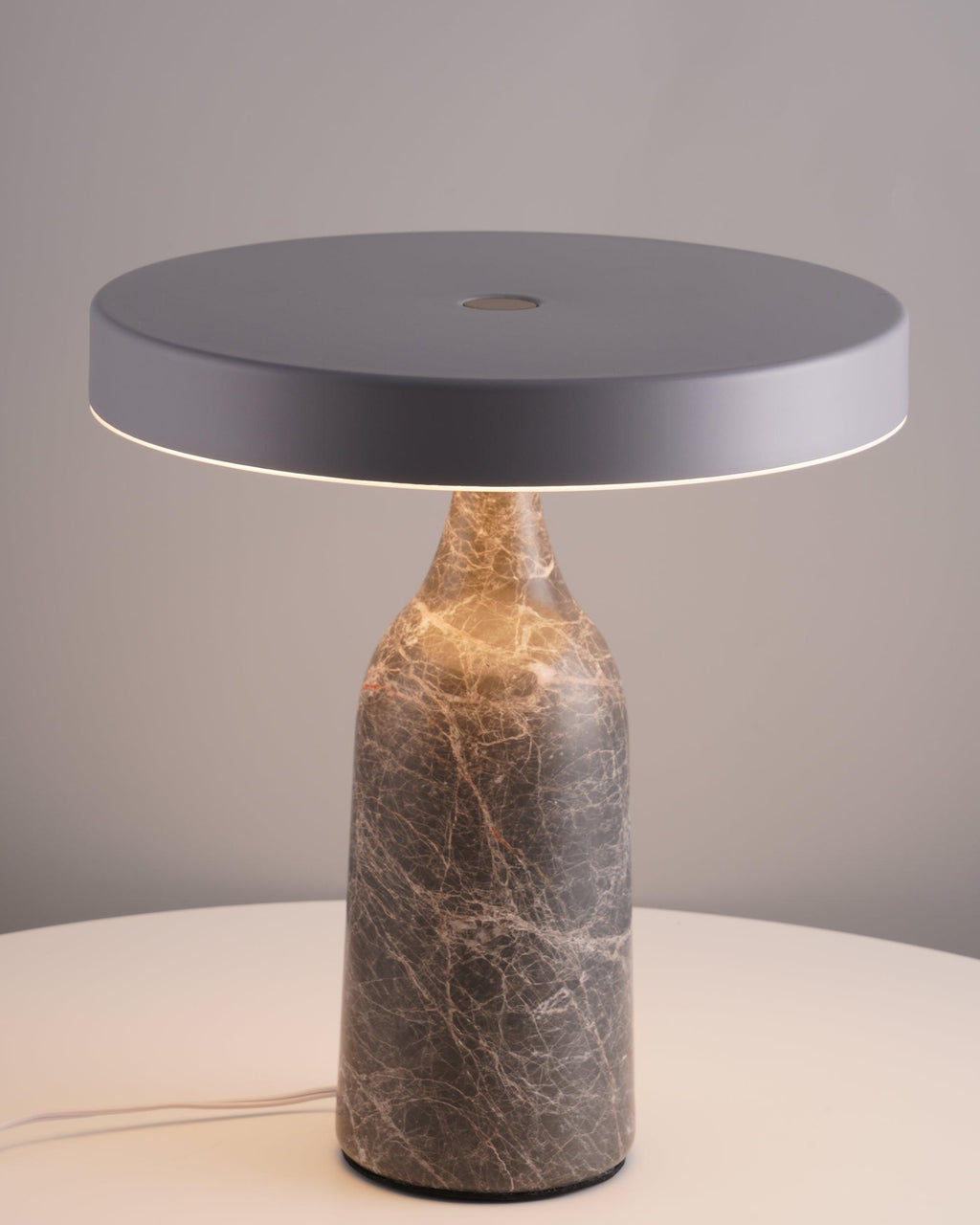 Photographed on a plain grey studio backdrop, this Clérachic lamp's grey marble base holds its disc shade level and unlit.
