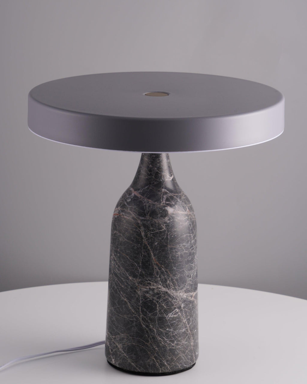 Set on a round white table against a grey backdrop, this Clérachic lamp's grey marble base holds its disc shade flat and unlit.