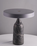 Set on a round white table against a grey backdrop, this Clérachic lamp's grey marble base holds its disc shade flat and unlit.