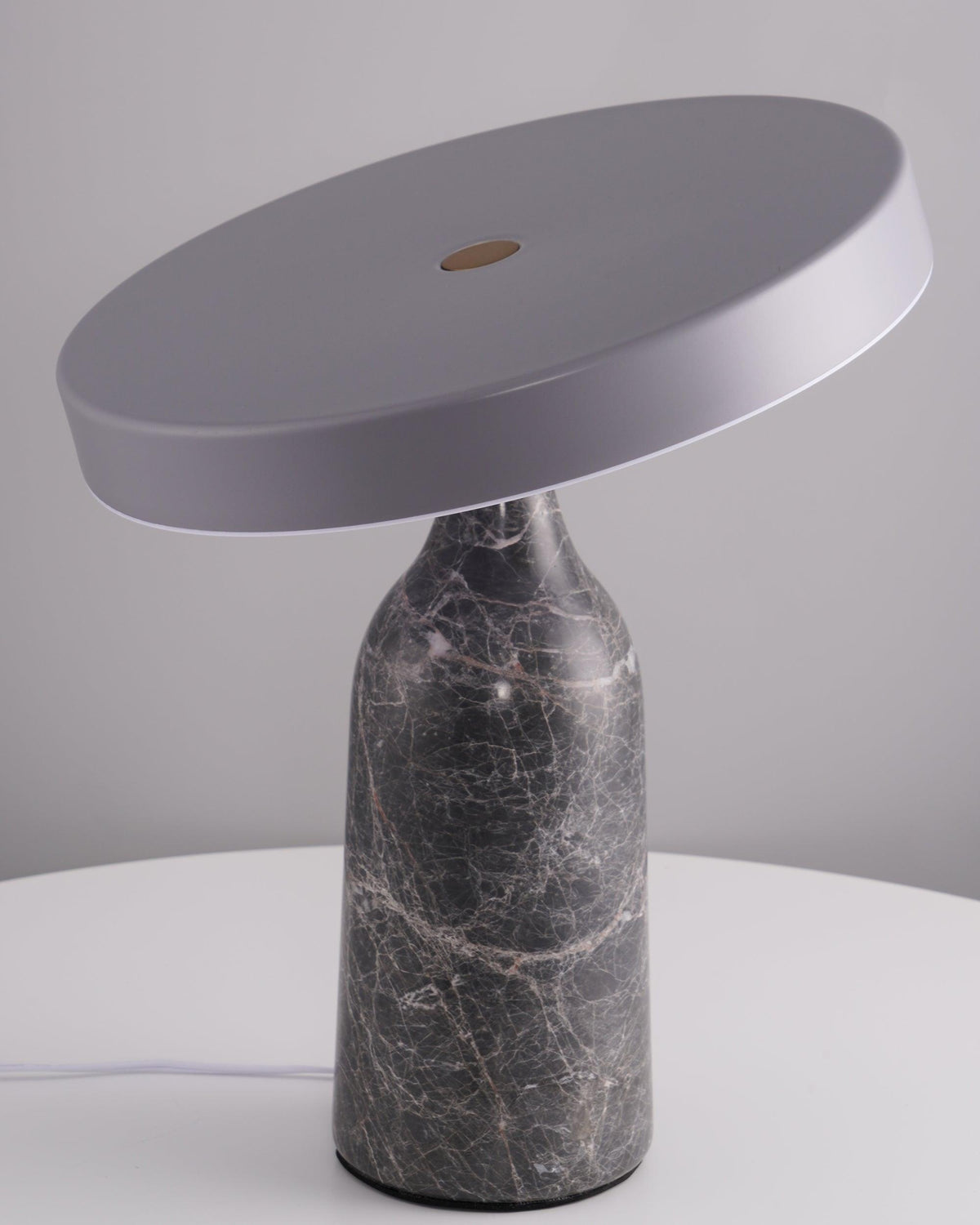 Photographed unlit against a plain grey backdrop, this Clérachic lamp's grey marble base supports its tilted disc, cord trailing to one side.