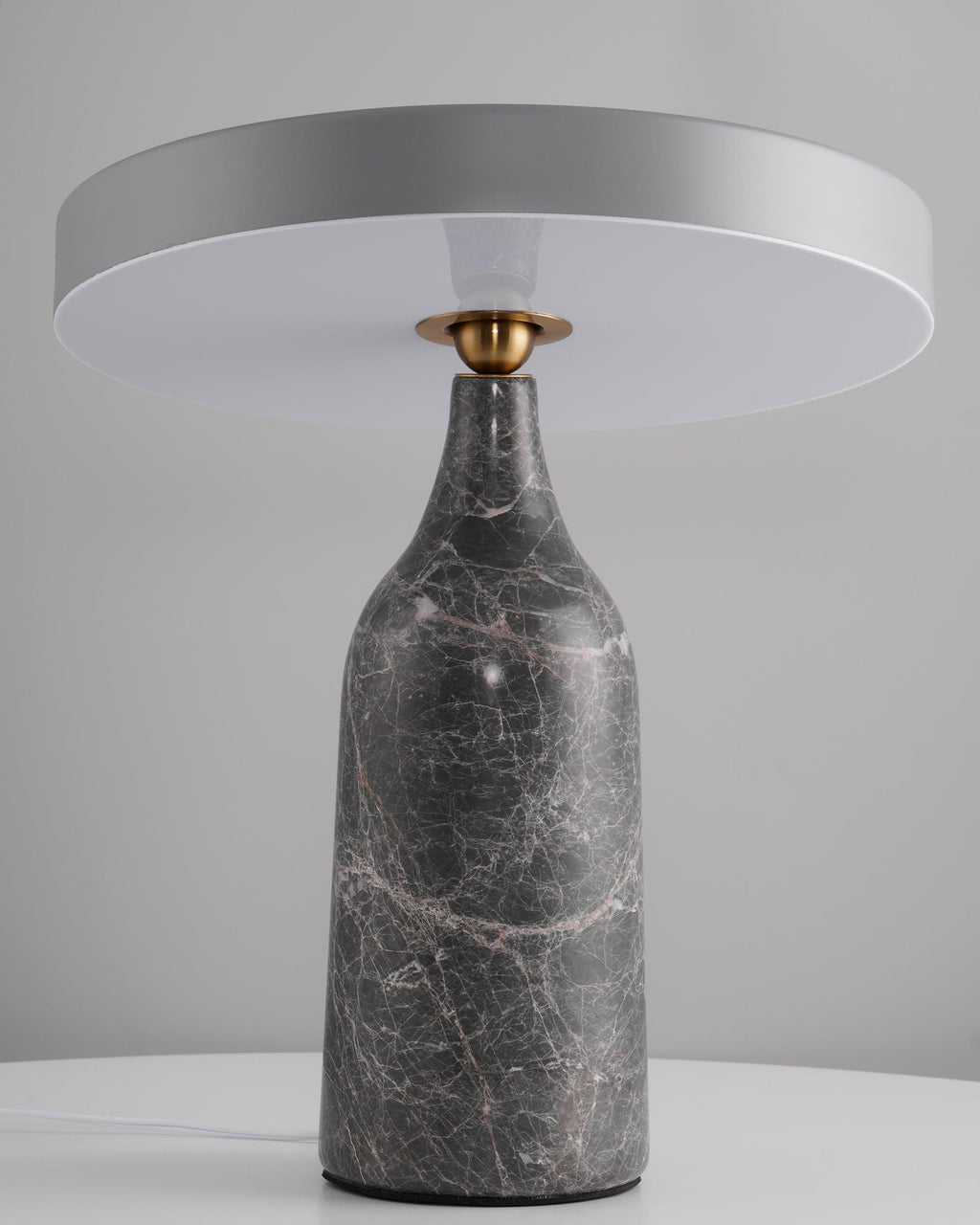 Sitting level on its grey marble base, the disc shade of this Clérachic lamp glows in a warm ring against a grey backdrop.