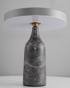 Sitting level on its grey marble base, the disc shade of this Clérachic lamp glows in a warm ring against a grey backdrop.