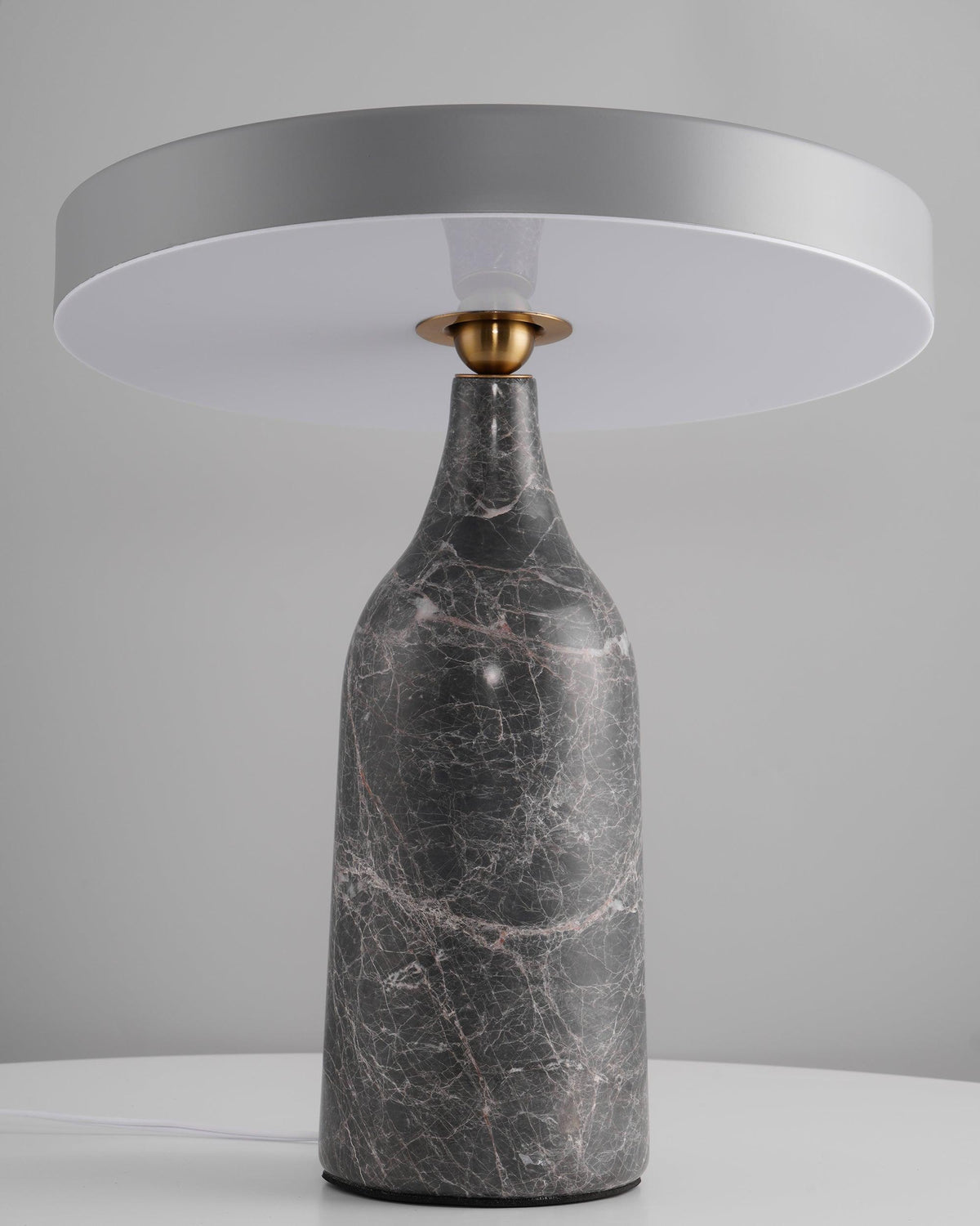 Sitting level on its grey marble base, the disc shade of this Clérachic lamp glows in a warm ring against a grey backdrop.