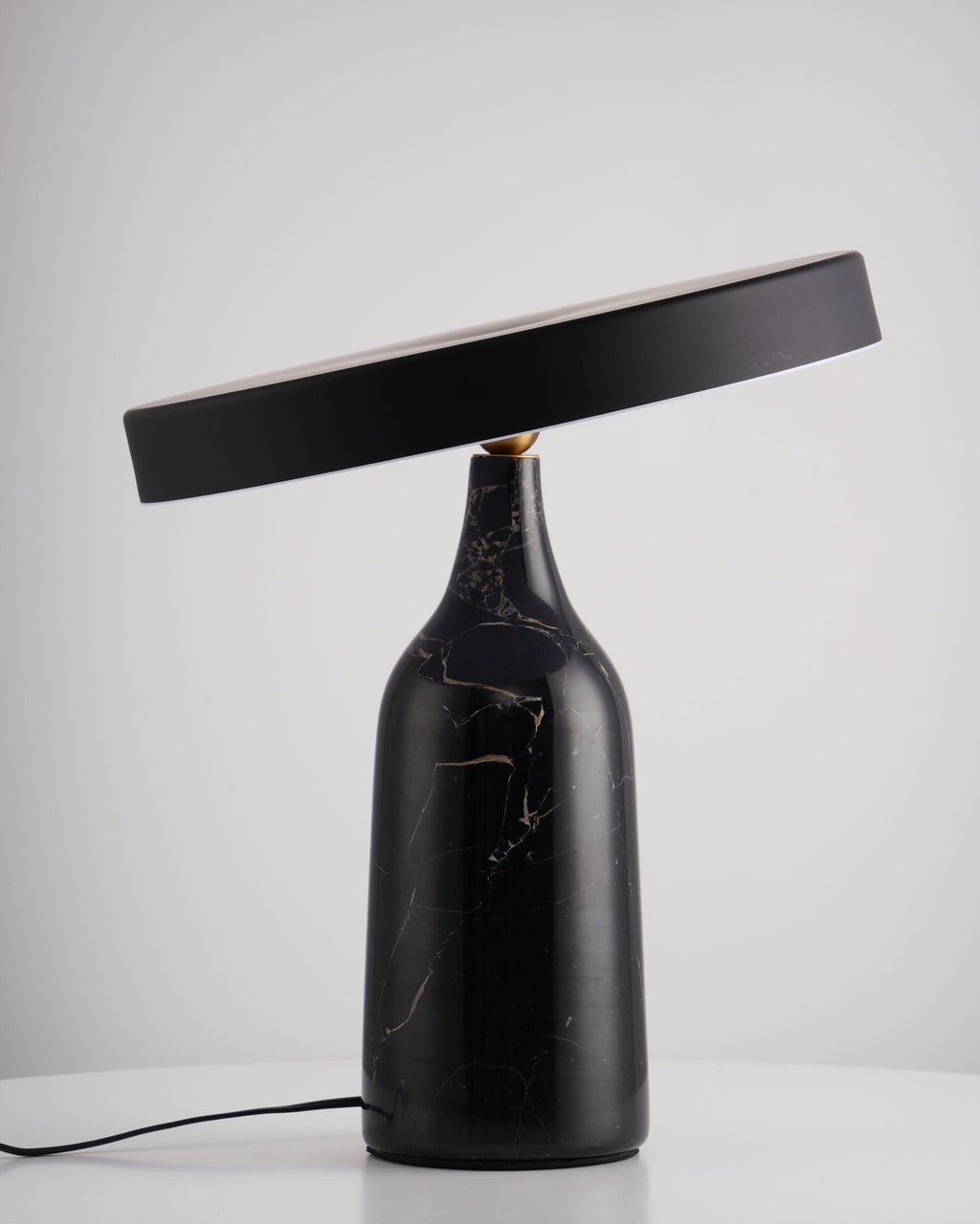 Tilted steeply on its black marble base, this Clérachic lamp's disc shade sits dark and unlit against a plain grey backdrop.