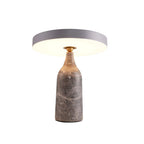Sitting level on the black marble base, this Clérachic lamp's disc shade glows warm in a ring, its cord visible on white.
