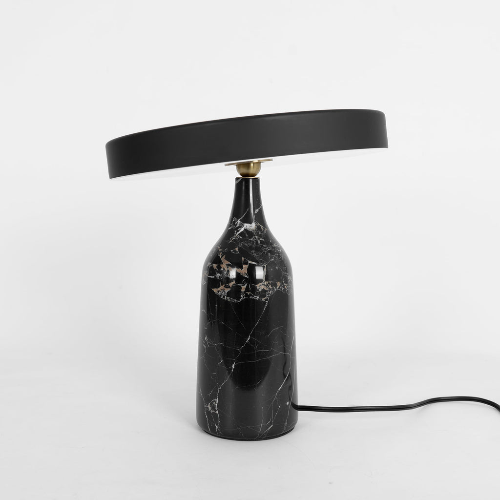 Black marble Clérachic table lamp, disc shade tilted, studio shot with the cord trailing off to the right.