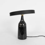 Black marble Clérachic table lamp, disc shade tilted, studio shot with the cord trailing off to the right.