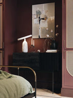 Grey marble Clérachic table lamp with its disc shade tilted steeply, beside pink roses and a dark blue sofa.