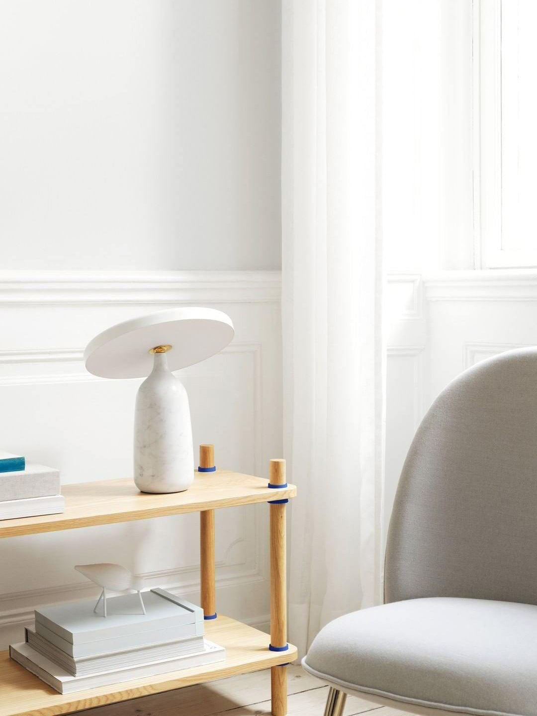 White marble Clérachic table lamp on the wooden shelf, photographed from a slightly wider angle near the window.