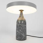 Grey marble Clérachic table lamp lit warm, its disc shade held level above the glowing base, tall studio crop.