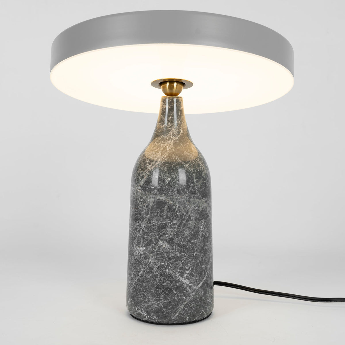 Grey marble Clérachic table lamp lit warm, its disc shade held level above the glowing base, tall studio crop.