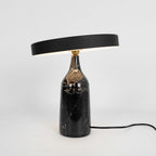 Black marble Clérachic table lamp, disc shade tilted, a similar studio shot with the cord trailing off to the left.