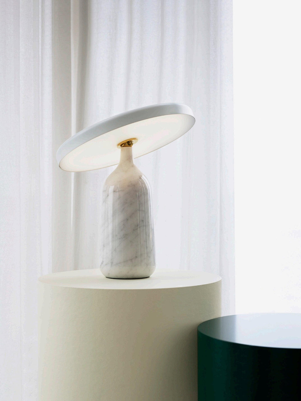 White marble Clérachic table lamp on the cream pedestal, a wider view showing the dark green stool alongside.