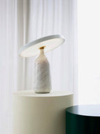 White marble Clérachic table lamp on the cream pedestal, a wider view showing the dark green stool alongside.