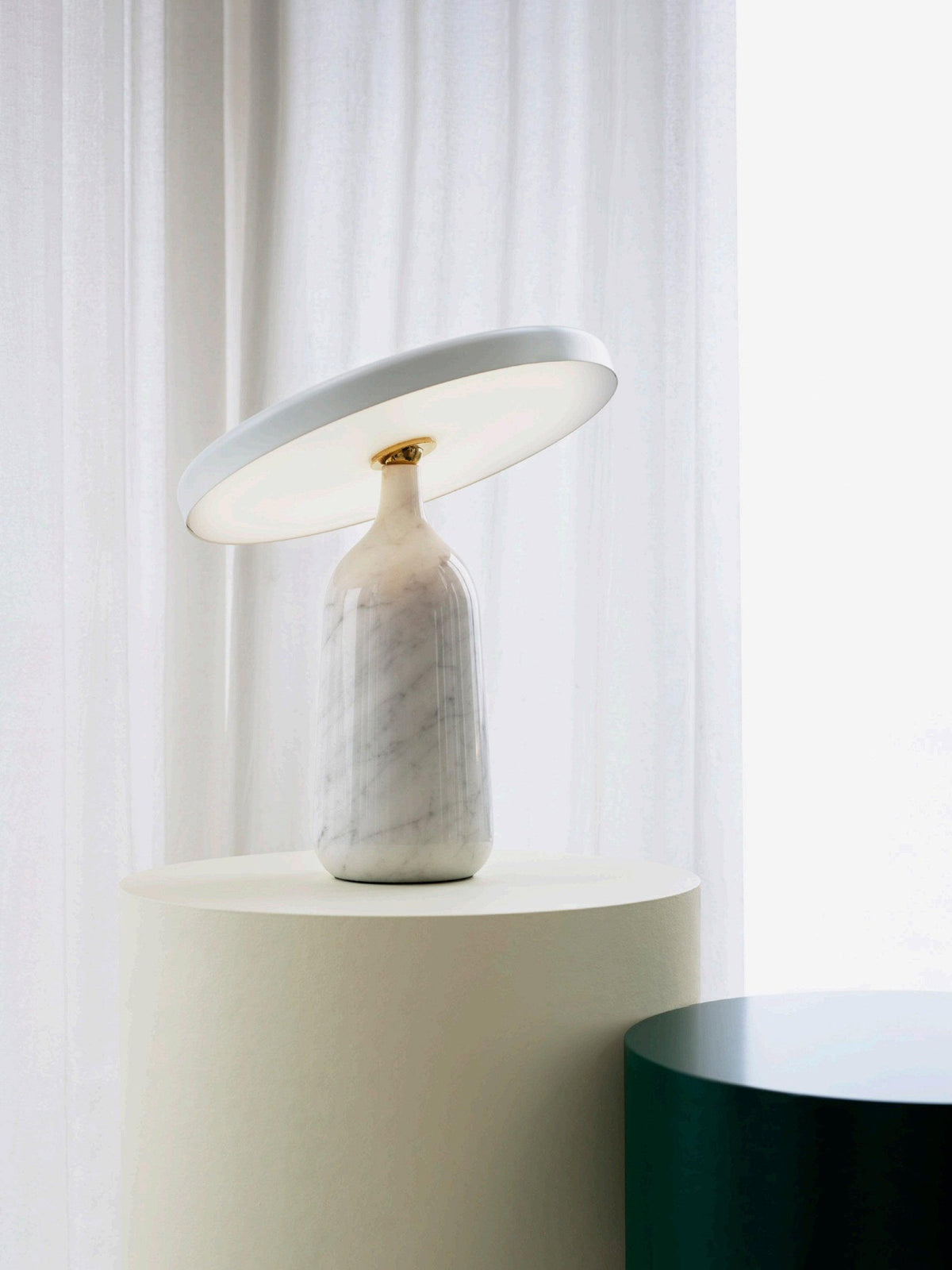 White marble Clérachic table lamp on the cream pedestal, a wider view showing the dark green stool alongside.
