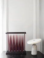 White marble Clérachic table lamp beside a dark red pleated decorative piece on a black table.