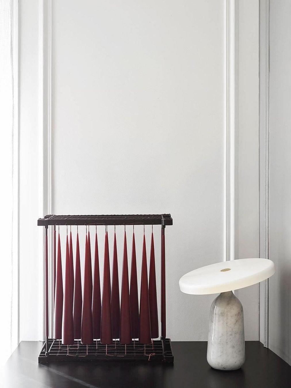 White marble Clérachic table lamp beside a dark red pleated decorative piece on a black table.