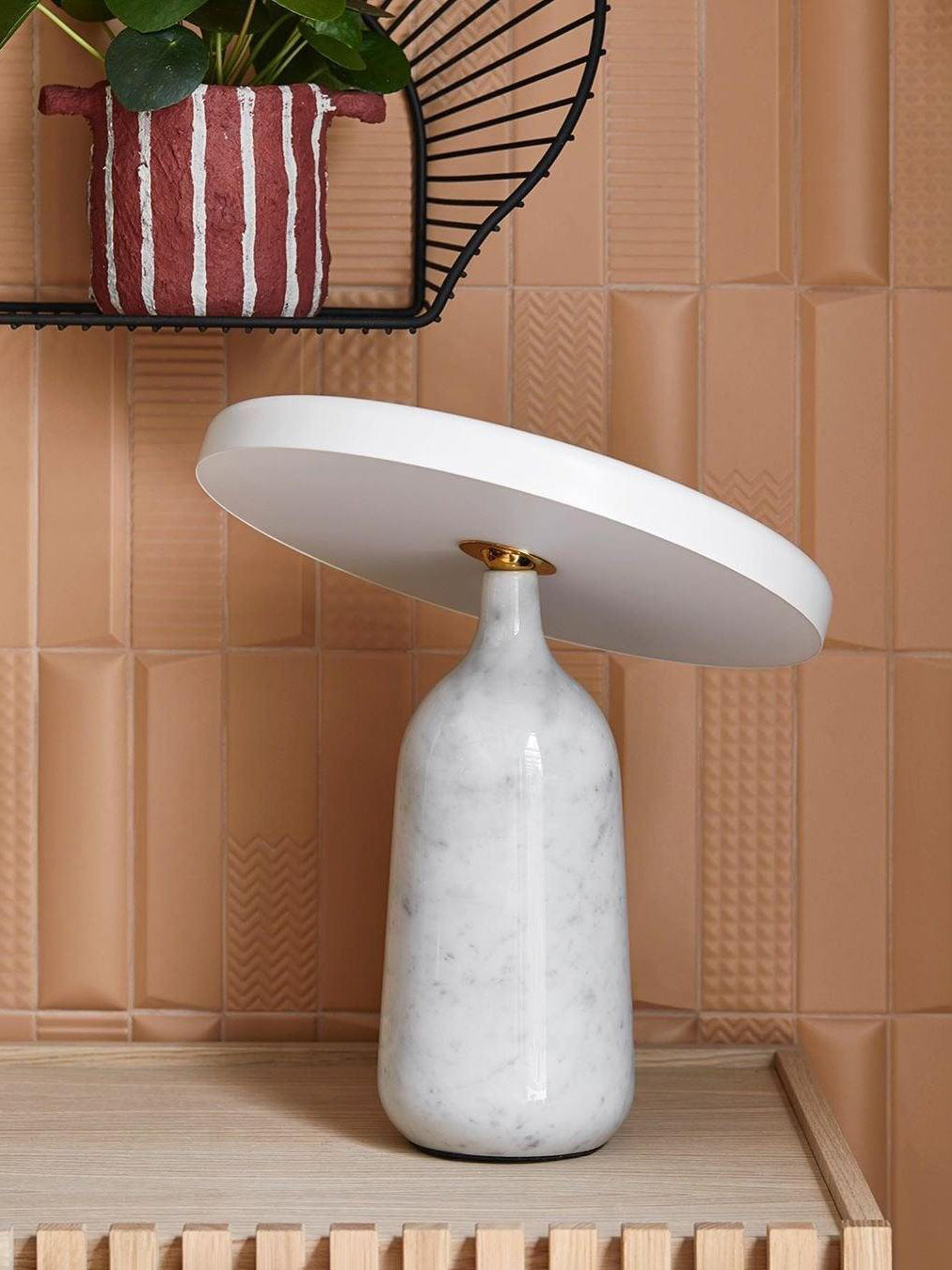 White marble Clérachic table lamp on a white sideboard in a bedroom, beside a framed photo and arch ornament.