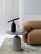A round-top pedestal side table from the Clérachic collection, styled with a dark lamp-like vase beside a tan sofa.