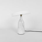 White marble Clérachic table lamp with its disc shade tilted steeply, cropped close with its cord visible.