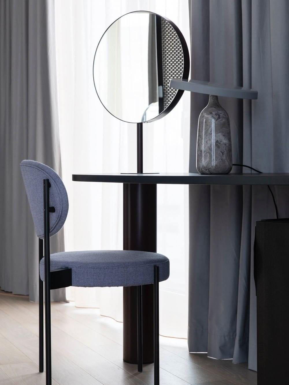 Grey marble Clérachic table lamp on a dark round table beside a round mirror and a blue upholstered chair.