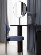 Grey marble Clérachic table lamp on a dark round table beside a round mirror and a blue upholstered chair.