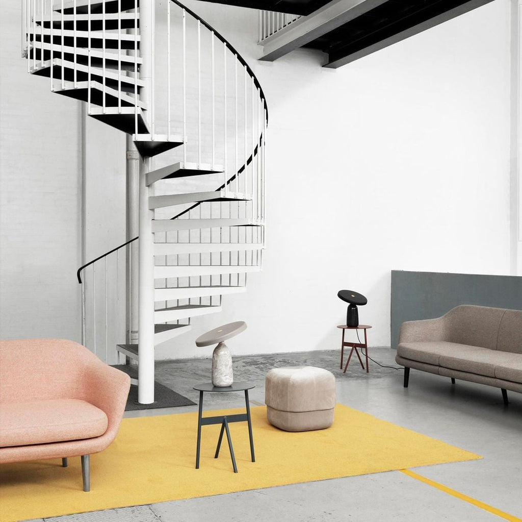 Wide view of a loft living room with a spiral staircase, a pink sofa and mustard rug, Clérachic table lamps on stands.