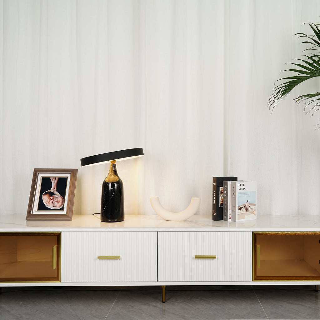Black marble Clérachic table lamp lit warm on a white sideboard, wider view with framed photo and books.