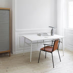 Grey marble Clérachic table lamp on a white desk in a bright room, beside stacked books and a tan chair.
