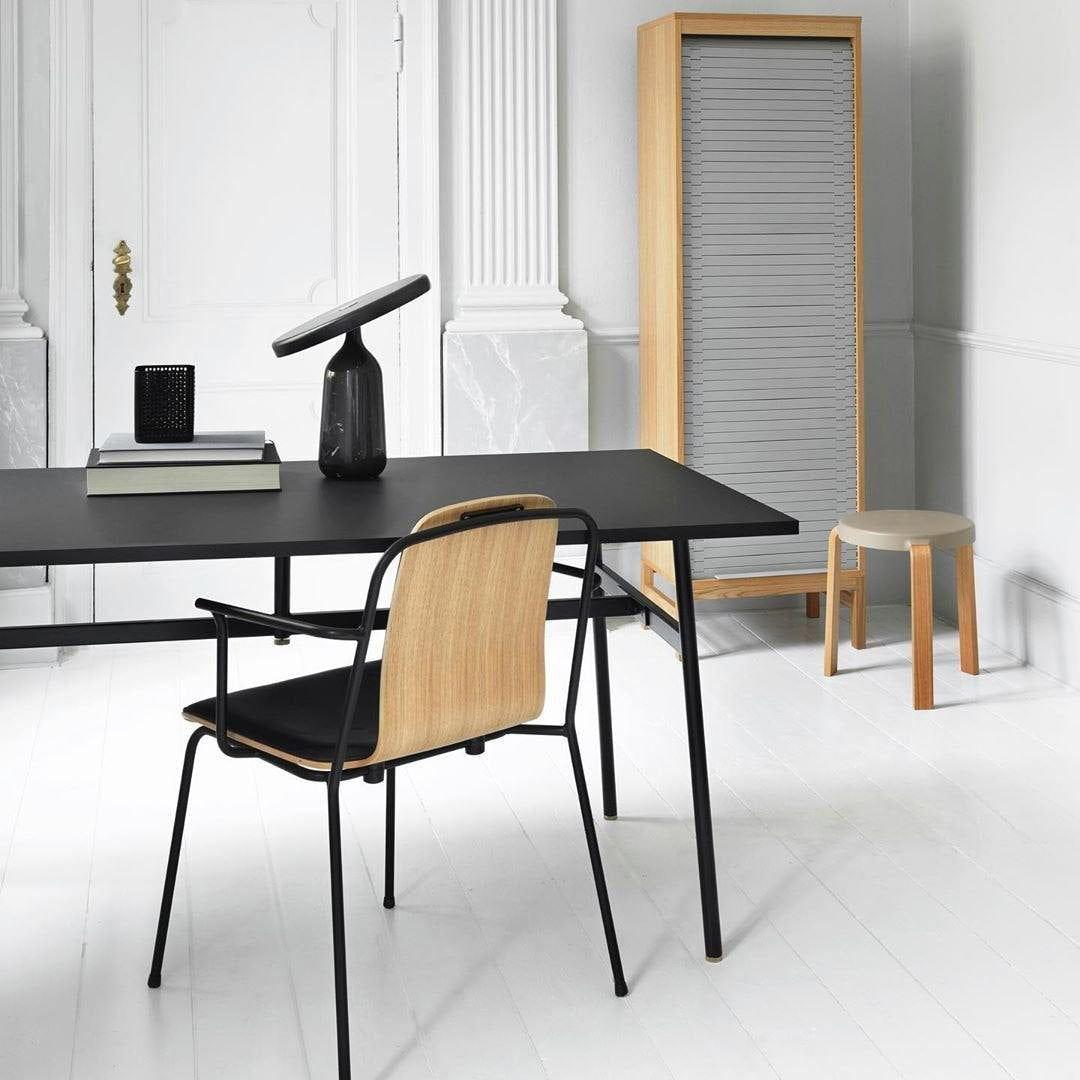 Black Clérachic table lamp on the black desk, photographed closer to show the disc shade above the bottle base.