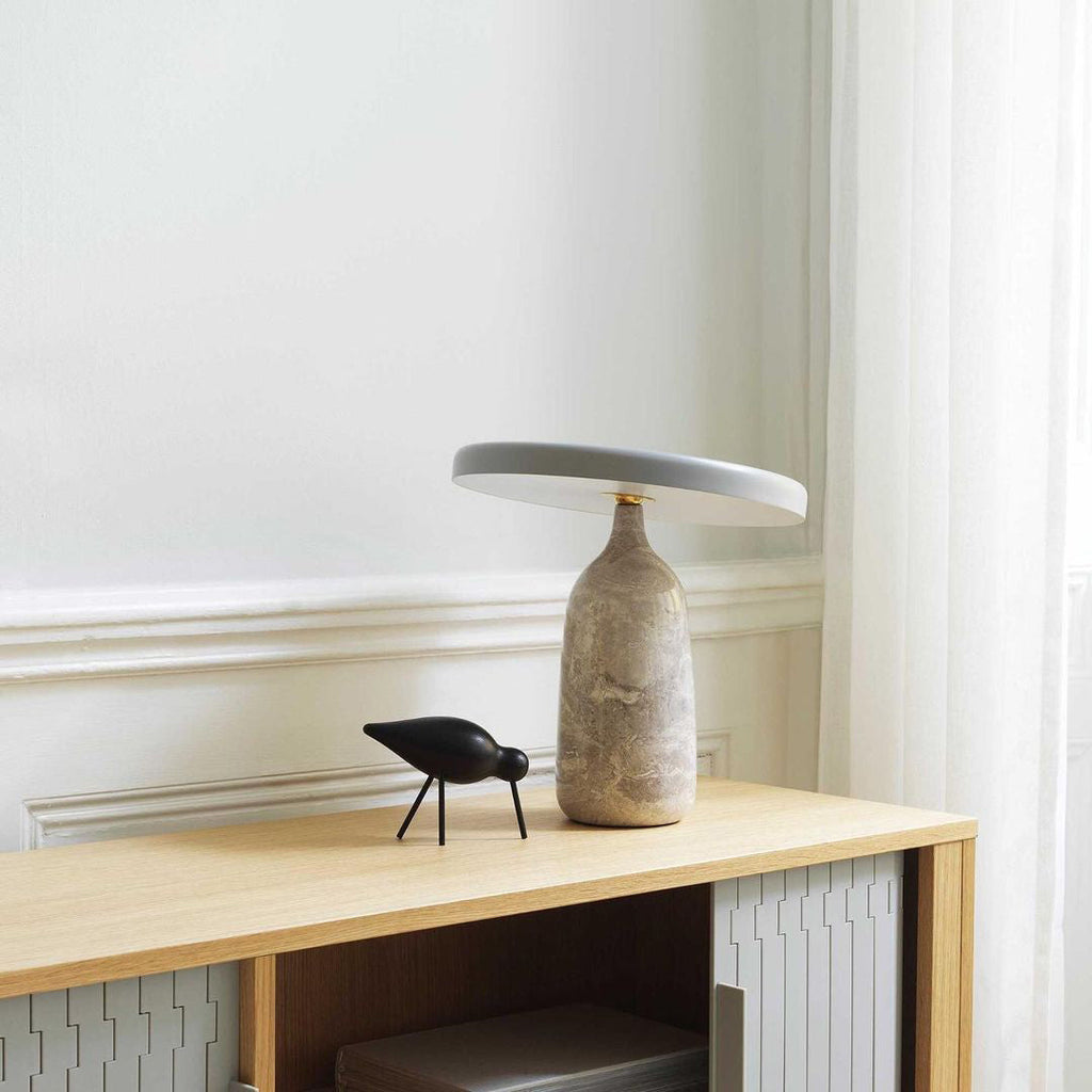 Clérachic table lamp on a wooden console beside a small black bird ornament, near a window with a radiator below.