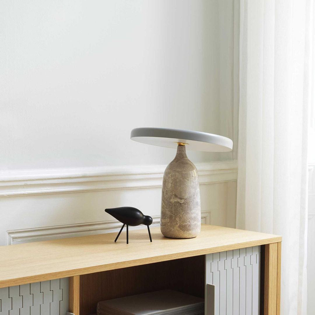 Clérachic table lamp on a wooden console beside a small black bird ornament, near a window with a radiator below.