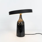 Black marble Clérachic table lamp with its disc shade held level, a clean studio shot with its cord visible.