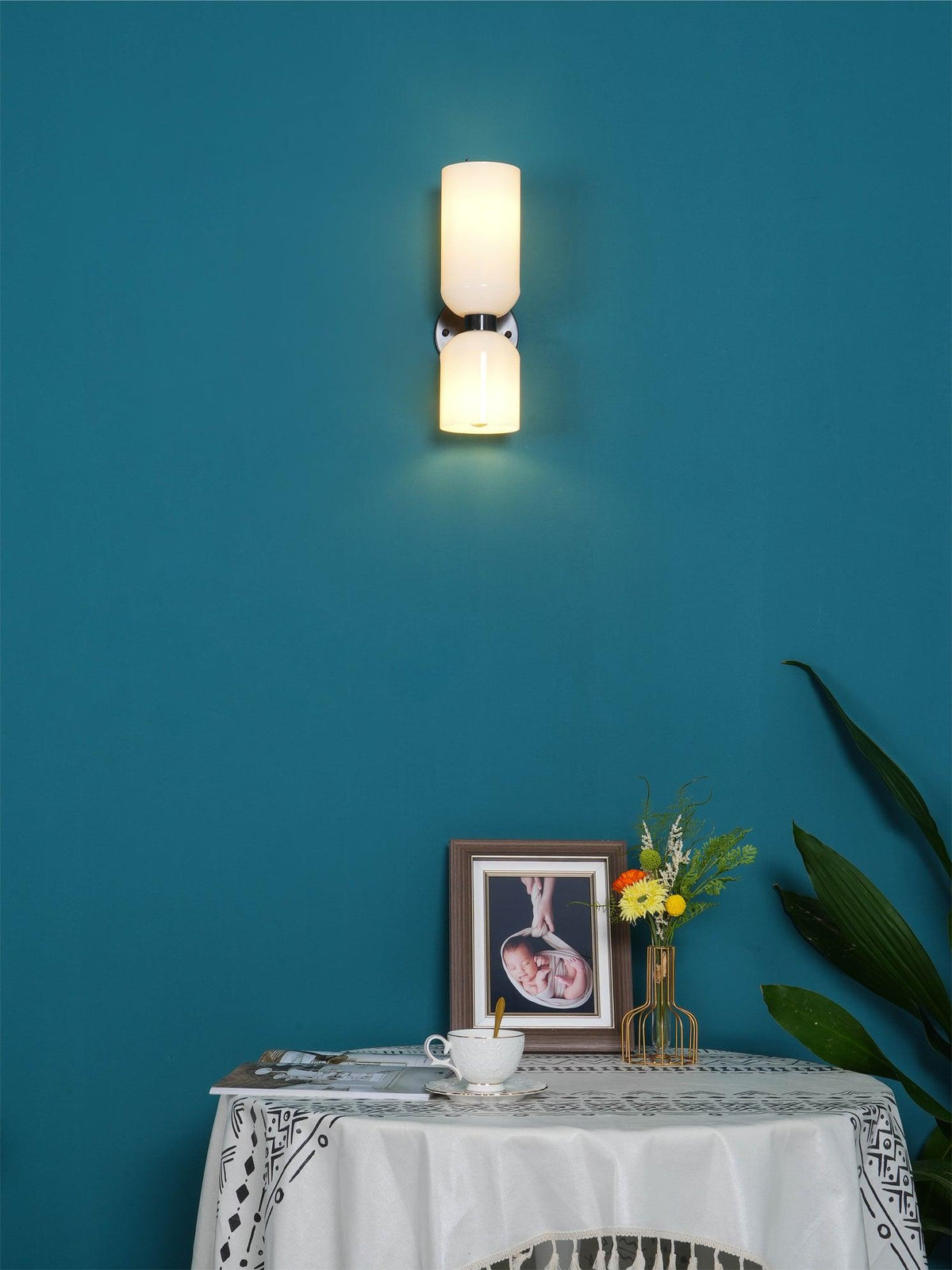 Above a table with a small plant, this matt black Clérachic wall light glows on a deep teal wall.