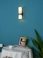 A teal wall sets off the glowing opal shades of this matt black Clérachic wall light above a table.