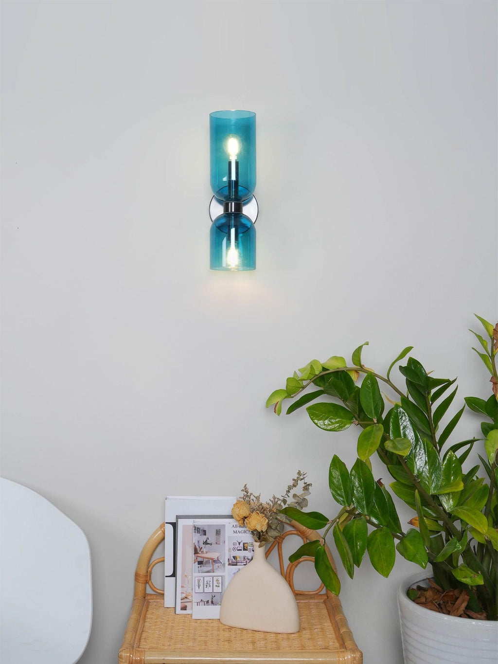 Near a small side table with magazines, this Clérachic wall light's blue glass shades glow softly.