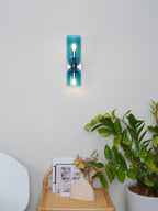 Near a small side table with magazines, this Clérachic wall light's blue glass shades glow softly.