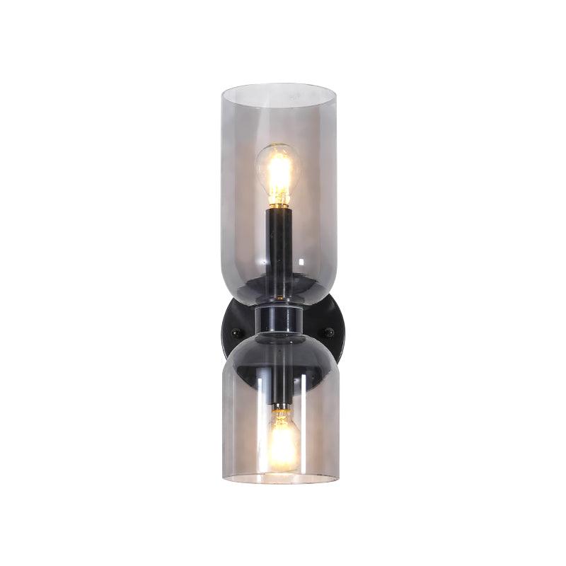 Both bulbs glow through the smoke grey glass of this matt black Clérachic sconce on white.