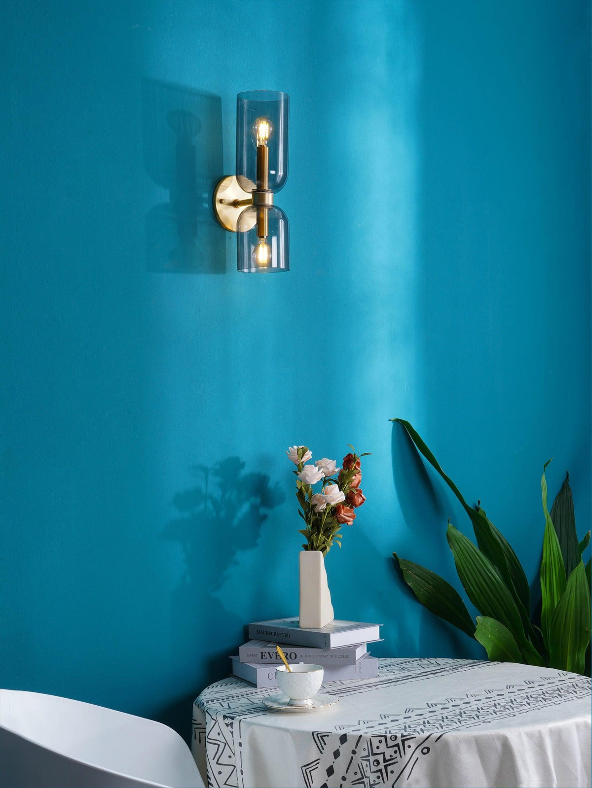 Above a table set with flowers and books, this gold Clérachic sconce glows on a teal wall.