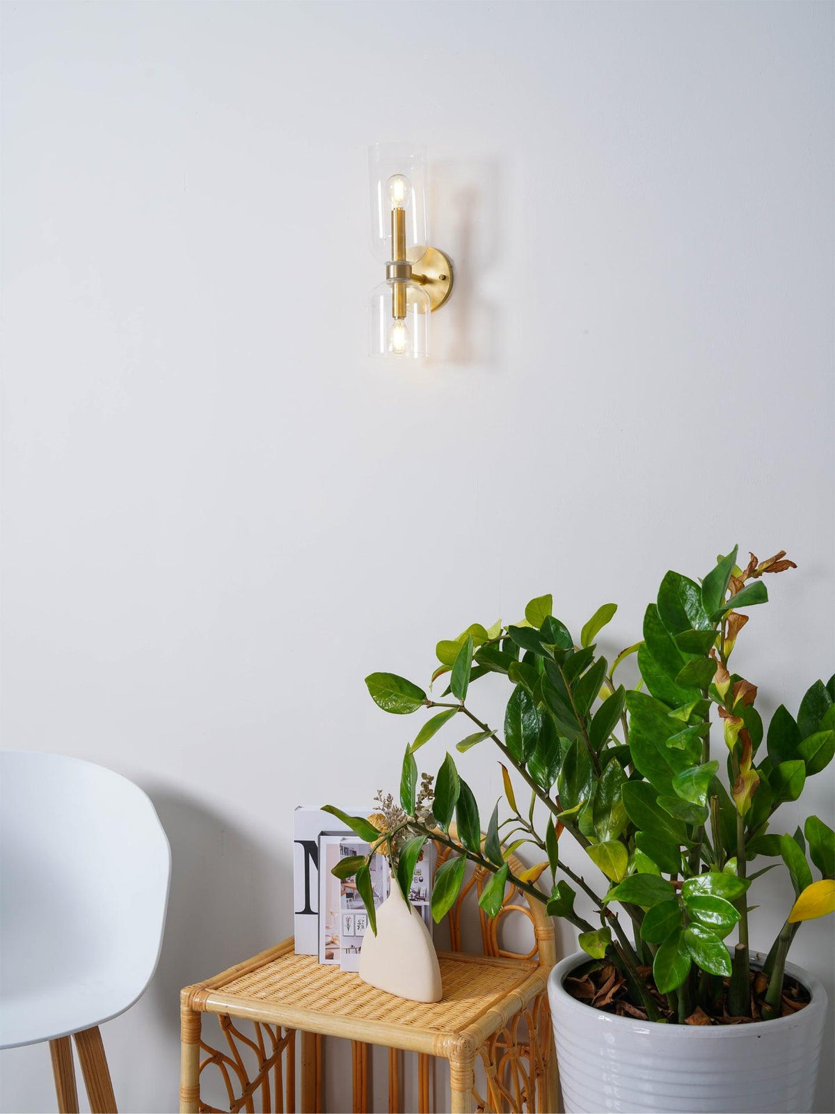 Potted plants sit beside this gold Clérachic wall light, its clear glass shades unlit on white.