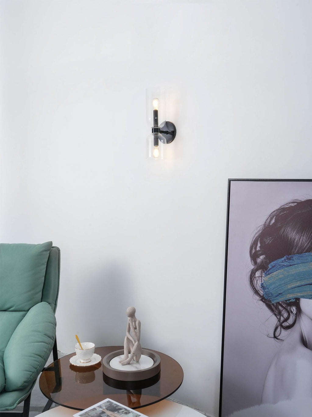 A distant view of this matt black Clérachic sconce beside a teal sofa and a framed portrait.