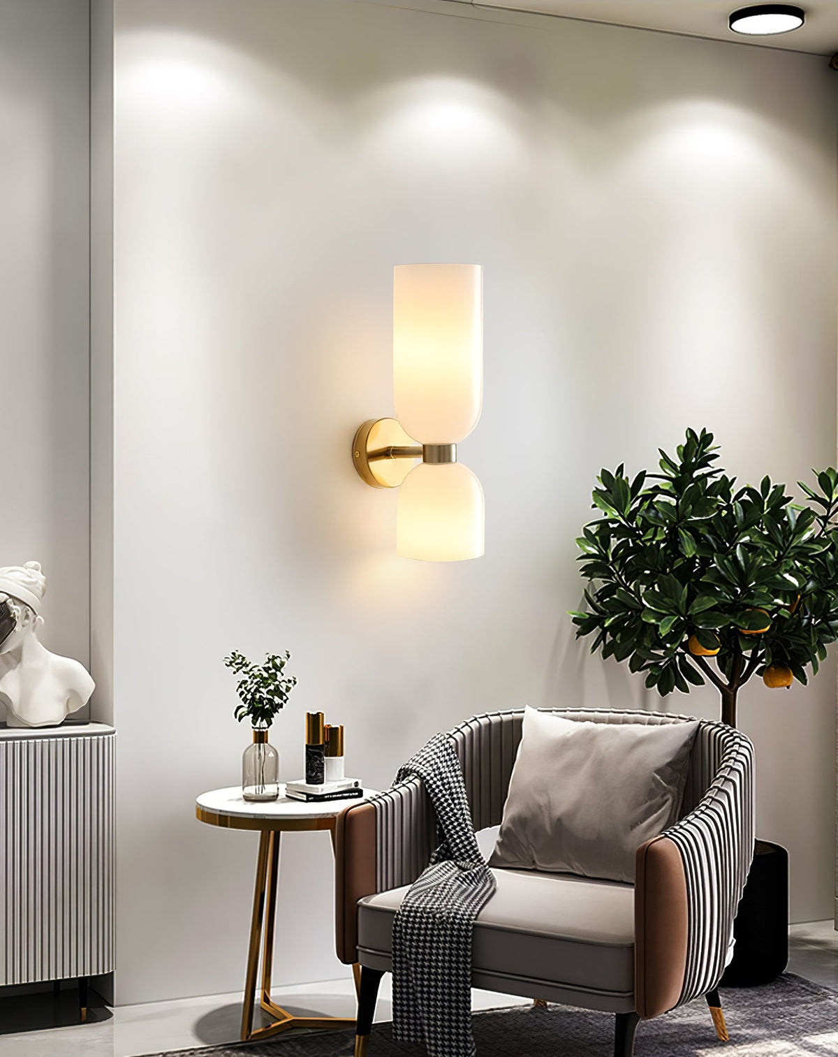 In a living room with a potted tree and armchair, this gold Clérachic sconce glows softly.