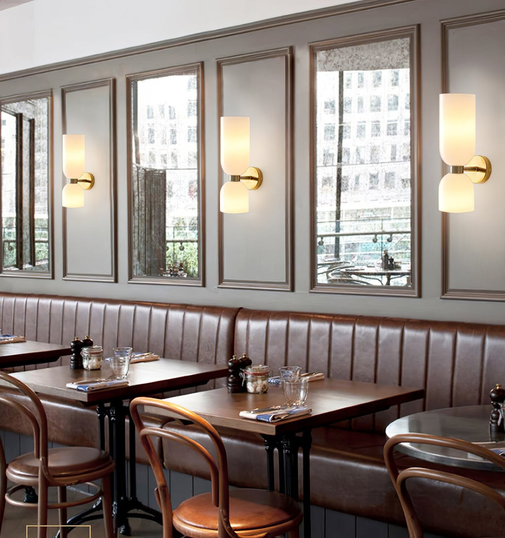 In a café setting, three gold Clérachic wall lights with opal shades line a mirrored wall above leather booths.