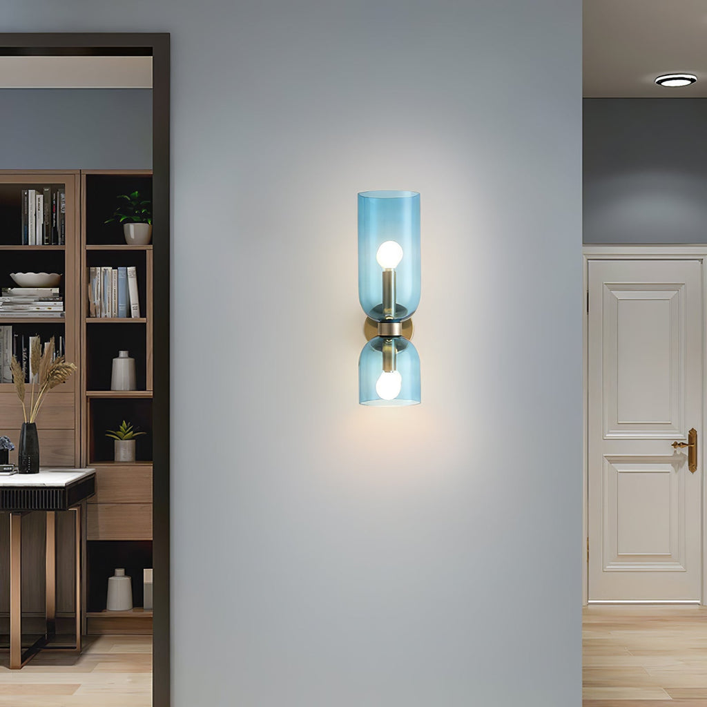 Blue glass cylinders on this gold Clérachic wall light glow in a hallway lined with a bookshelf.
