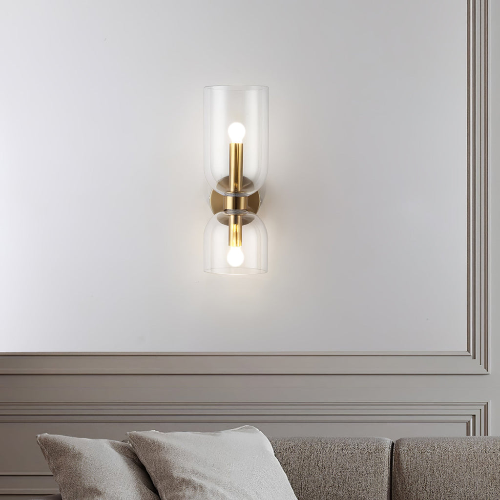 A clear-glass Clérachic sconce in gold lights a panelled wall above cushions in this living room.